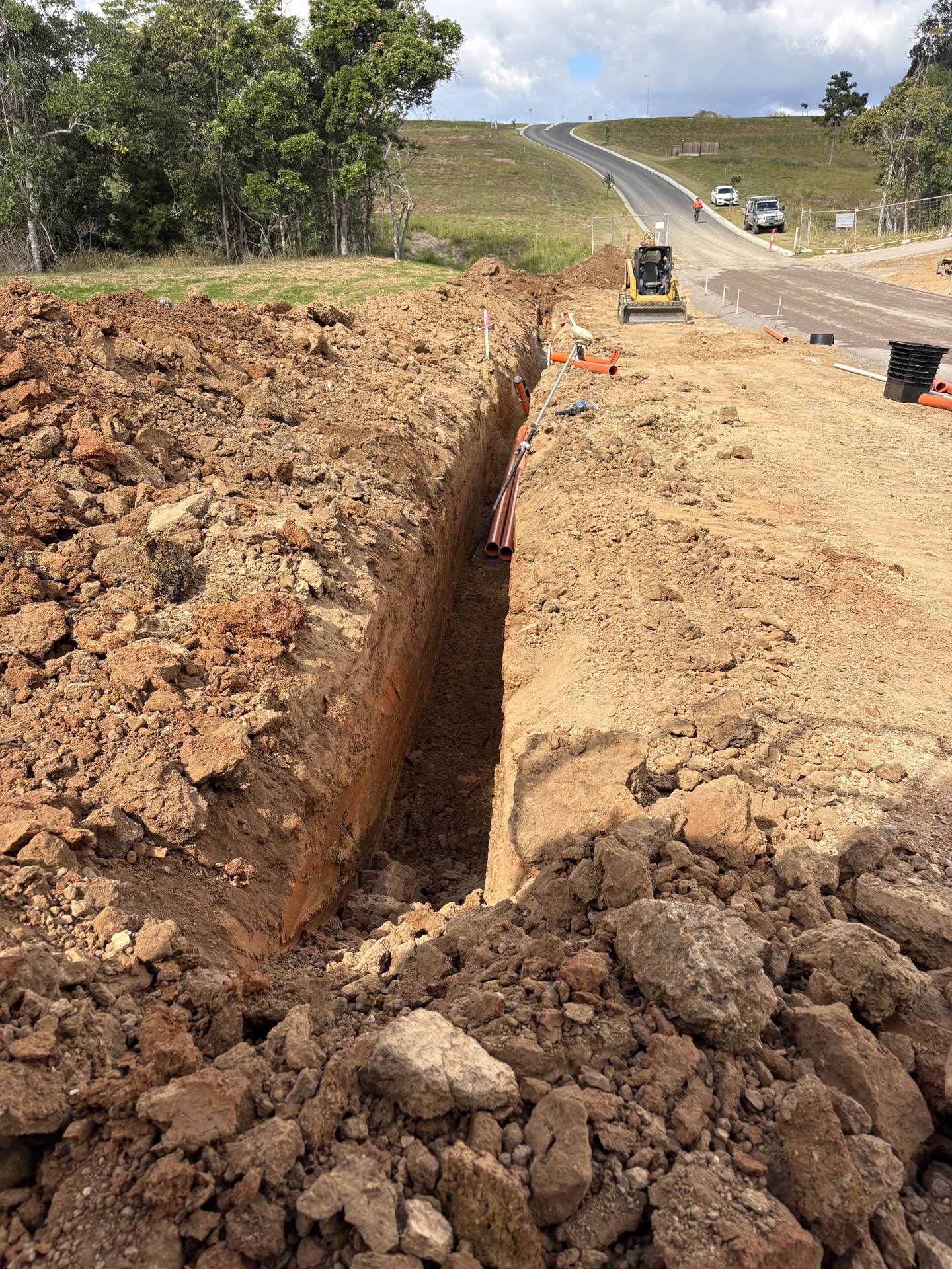 Excavator digging a service trench beside a new road at Pie Creek QLD