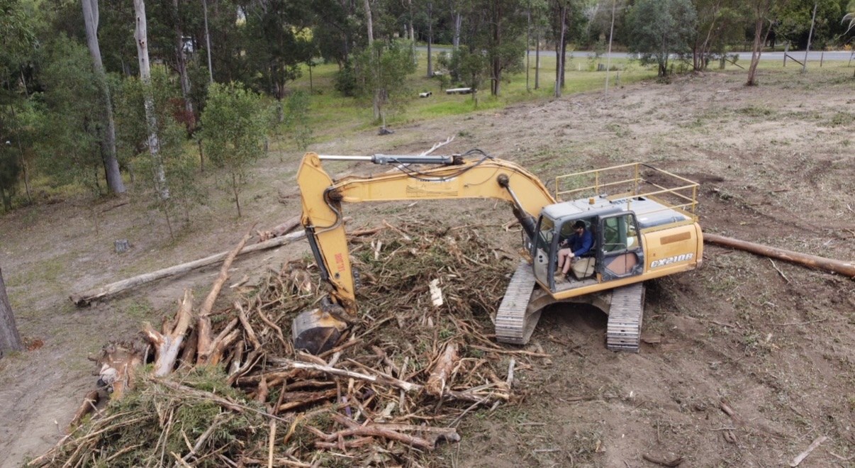 Excavator stacking cleared timber into a burn heap near Gympie QLD