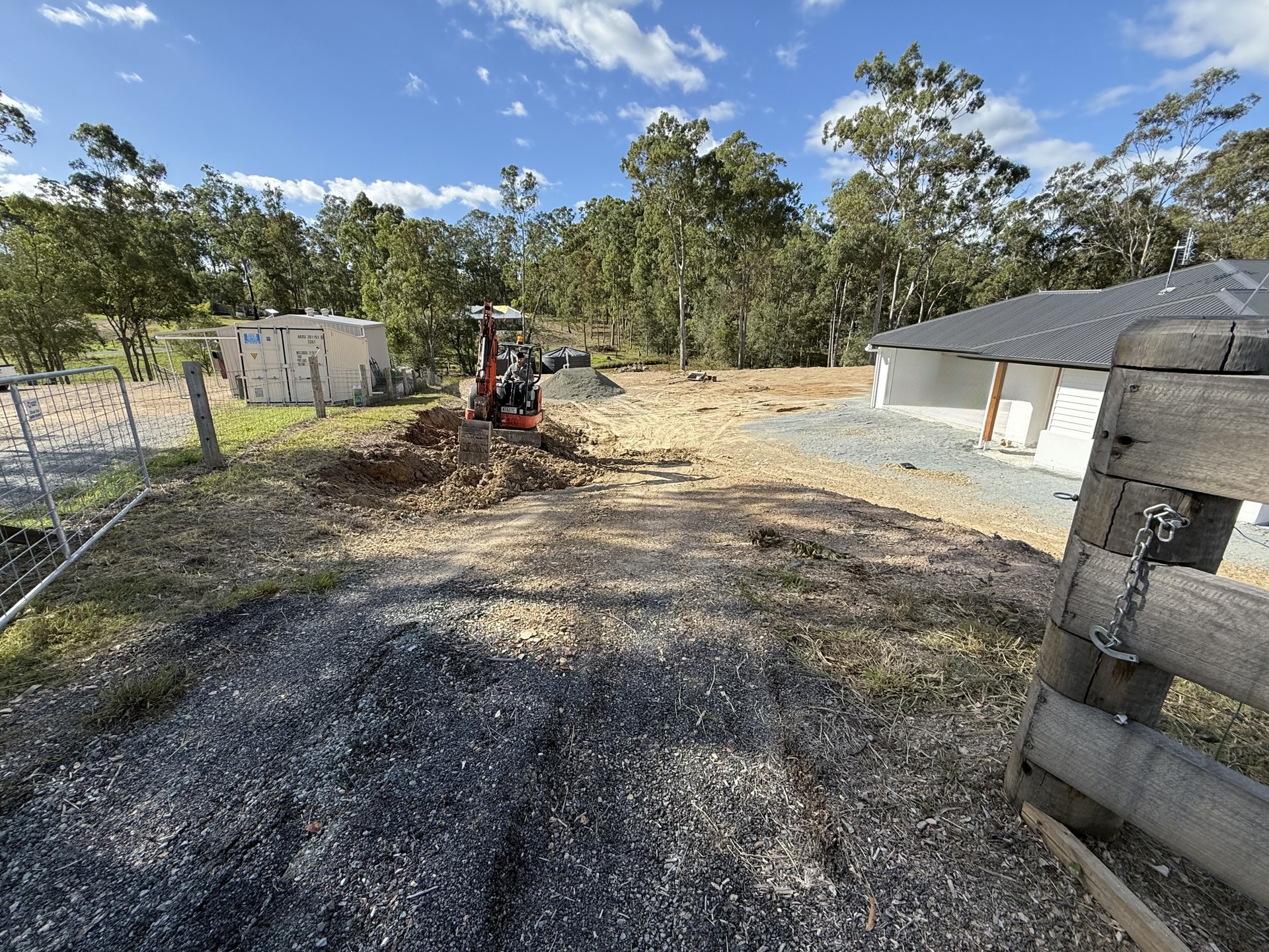 Mini excavator digging a drainage line beside a new driveway near Gympie QLD