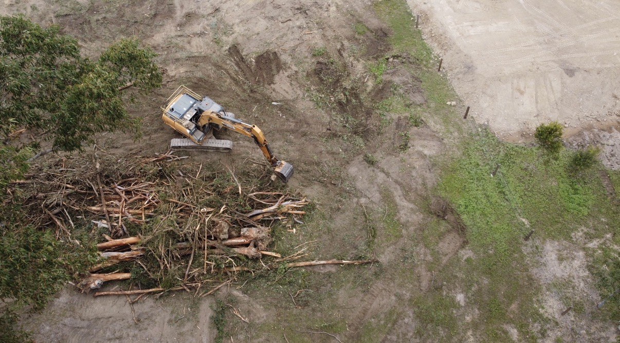 Aerial view of an excavator heaping cleared timber beside a rural yard near Gympie QLD