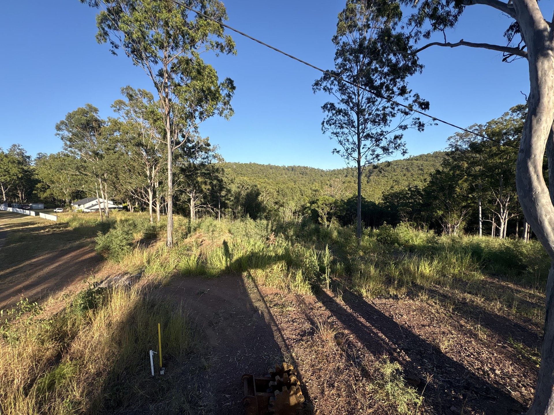 Sloping rural block with grass and timber before a house pad site cut at Glastonbury QLD